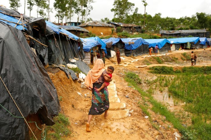 A Rohingya refugee woman walks on the muddy path as she carries a child at the Kutupalang Makeshift Refugee Camp in Cox's Bazar