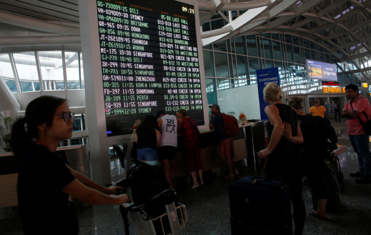 Passengers stand near the flight information board after Indonesian and regional authorities heightened flight warnings, following the eruption of Bali's Mount Agung volcano at Ngurah Rai International airpot in Bali