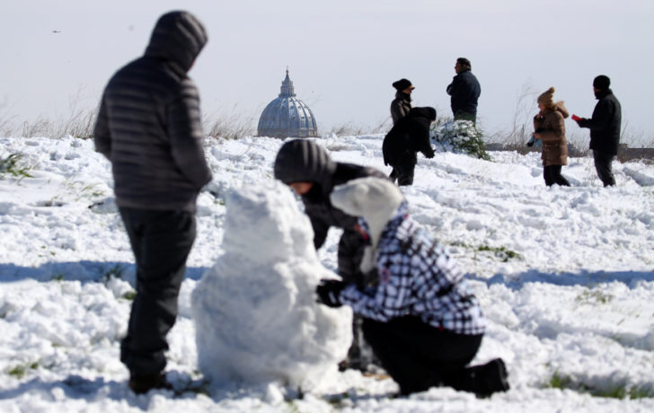 Saint Peter's Basilica is seen in the background as people enjoy the snow following a heavy snowfall at the Circus Maximus in Rome