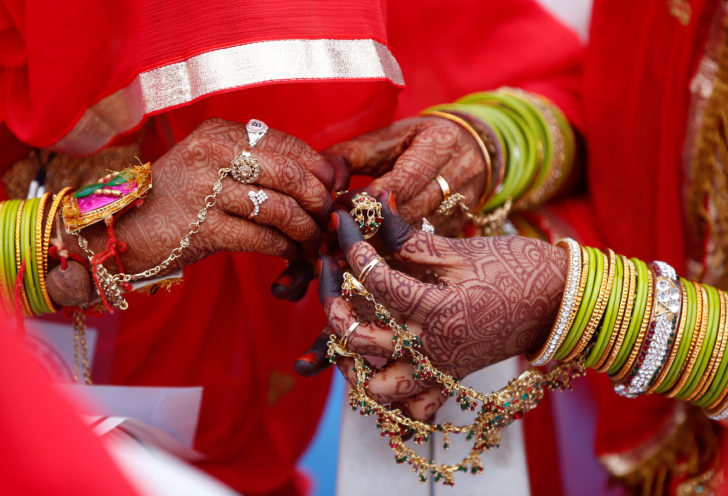 A bride helps another to wear her ornaments during a mass marriage ceremony in which, according to its organisers, 70 Muslim couples took their wedding vows, in Ahmedabad