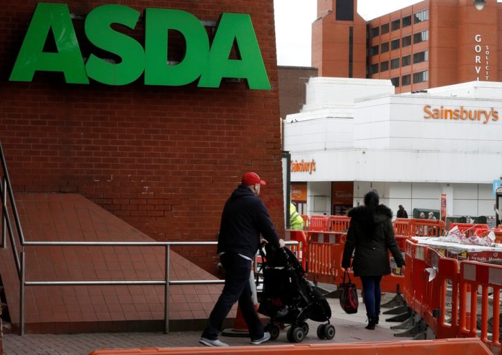 People walk past branches of ASDA and Sainsbury's in Stockport. “เซนส์บิวรี่ส์” ซื้อบริษัทลูก “วอลมาร์ท” กว่า 1 หมื่นล้านดอลล์ เพื่อสร้างซุปเปอร์มาร์เก็ตชั้นนำ