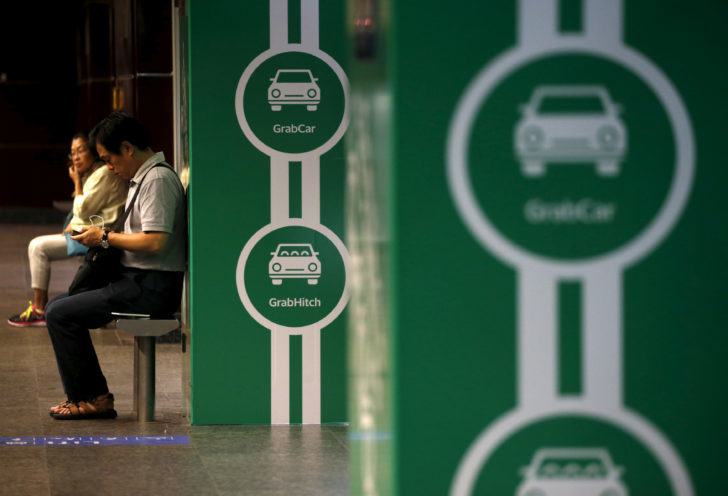FILE PHOTO: Commuters wait for a train next to Grab transport booking service app advertisements at a train station in Singapore