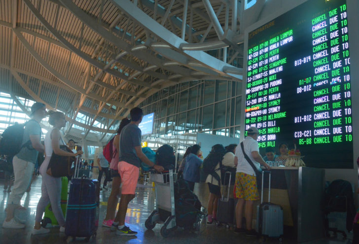 Airplane passengers stand in front of flight board as their flight was canceled due to Mount Agung eruption at Ngurah Rai airpot in Denpasar