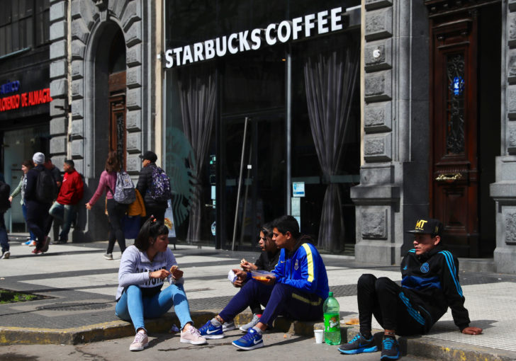 People eat a free meal from a soup kitchen set up on a street, as they sit in front of a Starbucks coffee shop, during a demonstration against the government’s economic measures in Buenos Aires