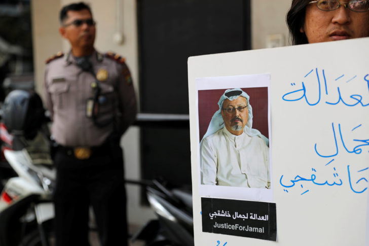 A policeman stands guard as an Indonesian journalist holds a placard during a protest over the disappearance of Saudi journalist Jamal Khashoggi in front of the Saudi Arabia embassy in Jakarta