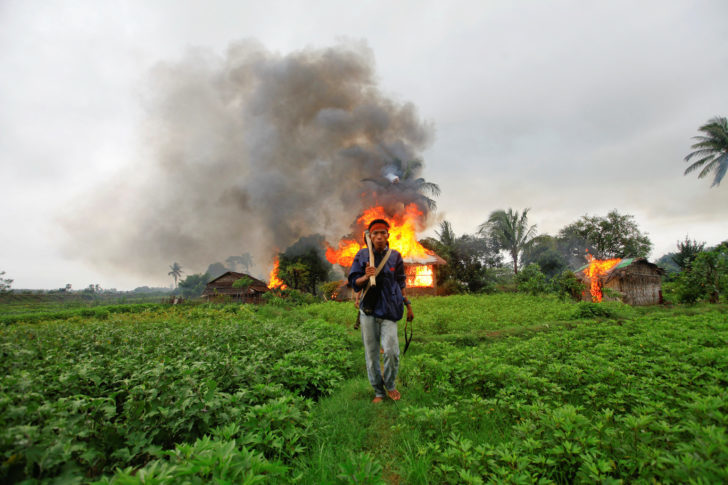 FILE PHOTO: An ethnic Rakhine man holds homemade weapons as he walks in front of houses that were burnt during fighting between Buddhist Rakhine and Muslim Rohingya communities in Sittwe