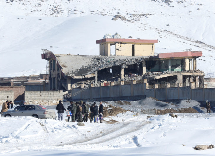 Afghan men stand in front of a collapsed building of a military base after a car bomb attack in Maidan Wardak