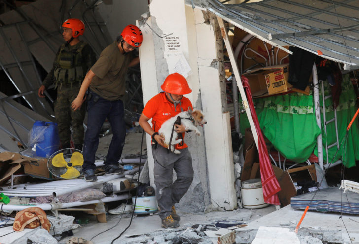A rescuer carries a search dog as they try to reach survivors at a collapsed four-storey building following an earthquake in Porac town