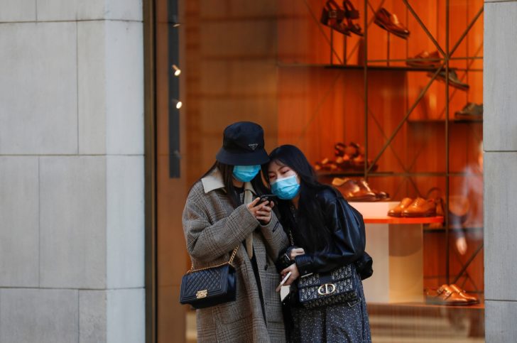 Women look on the phone in an empty Via Monte Napoleone street, as a coronavirus outbreak in northern Italy continues to grow, in Milan