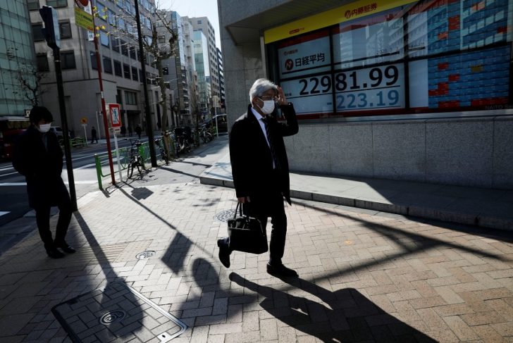 People wearing surgical masks walk past a screen showing Nikkei index outside a brokerage in Tokyo ตลาดญี่ปุ่นหดตัว “คนกลัวใช้จ่าย” “อาเบะโนมิกส์” สะดุด