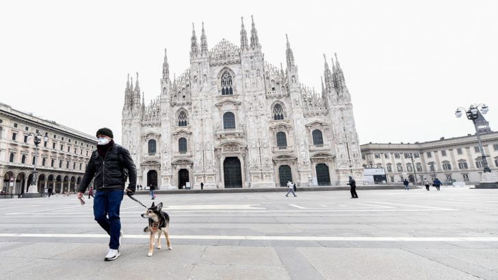 A man wearing a protective face mask walks a dog in Duomo square after a decree orders for the whole of Italy to be on lockdown in an unprecedented clampdown aimed at beating the coronavirus, in Milan