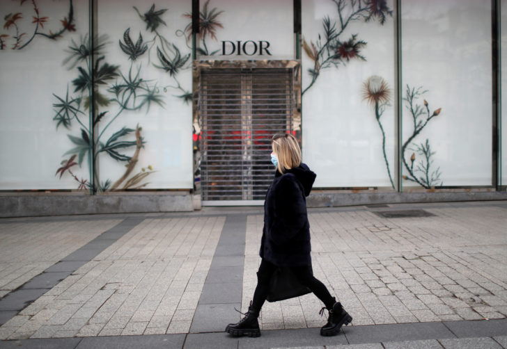 A woman wearing a protective face mask walks past the closed Dior shop on the Champs Elysees in Paris