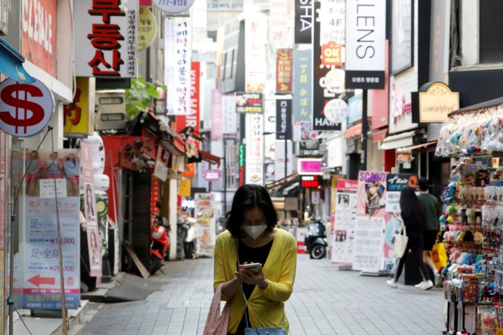 FILE PHOTO: A woman wearing a mask looks at her mobile phone amid social distancing measures to avoid the spread of the coronavirus disease (COVID-19), in Myeongdong shopping district in Seoul