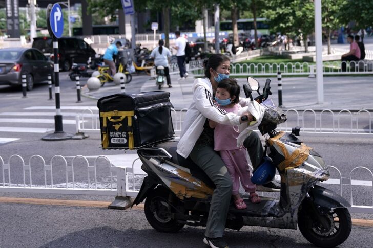 Delivery worker carries a child on her scooter as she rides past an office and commercial complex in Beijing's Central Business District (CBD)