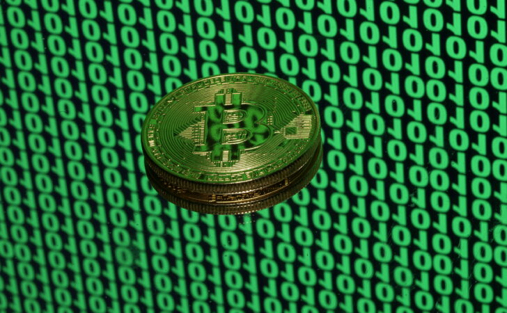 FILE PHOTO: Bitcoin token is seen placed on a monitor that displays binary digits in this illustration picture