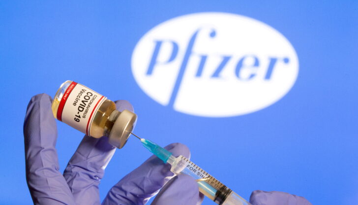 FILE PHOTO: FILE PHOTO: A woman holds a small bottle labeled with a 'Coronavirus COVID-19 Vaccine' sticker and a medical syringe in front of displayed Pfizer logo in this illustration