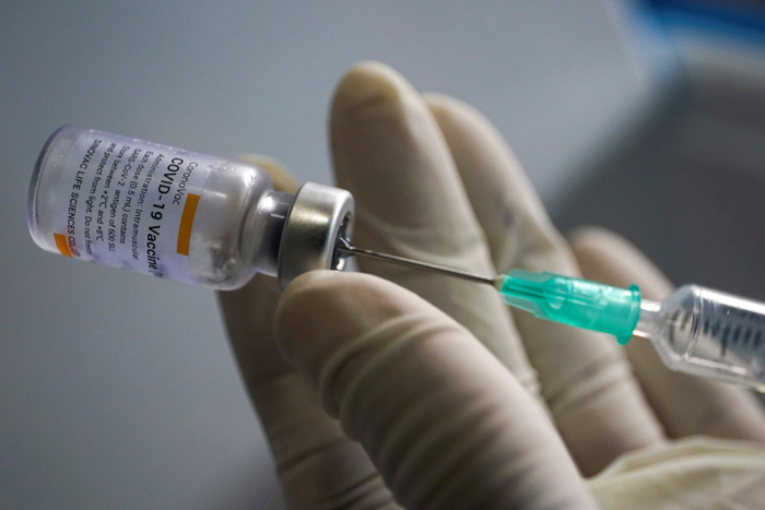 FILE PHOTO: A health worker holds a syringe and a vial of the Sinovac coronavirus disease (COVID-19) vaccine at a market in Bangkok