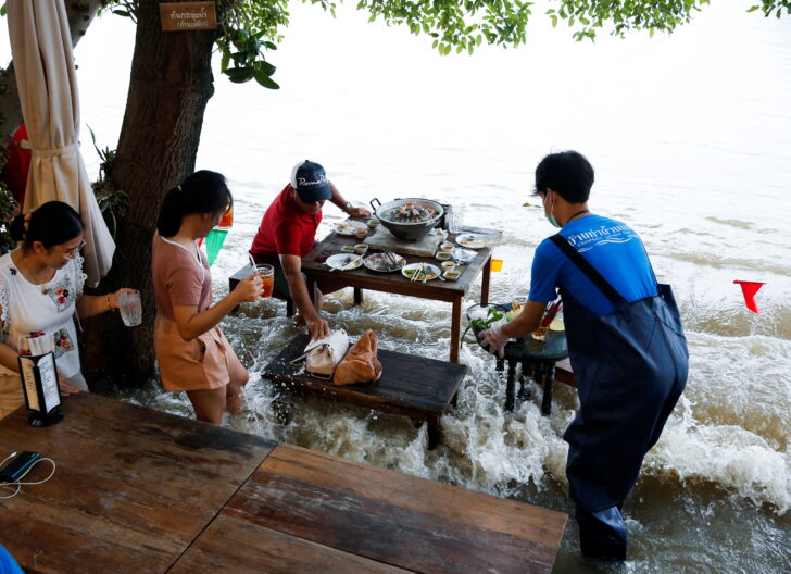 People eat food at a flooded restaurant, where patrons stand up from their tables every time the waves come in, on a river bank in Nonthaburi