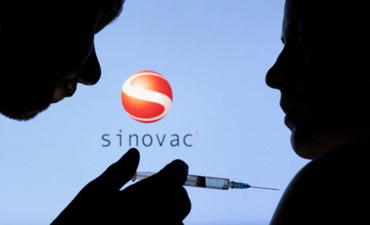 People pose with syringe with needle in front of displayed Sinovac logo