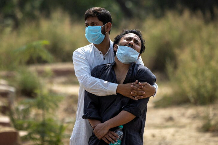 FILE PHOTO: A man is consoled by a relative before his father's burial at a graveyard in New Delhi WHO เผยตายจากโควิดทั่วโลก 15 ล้านคน