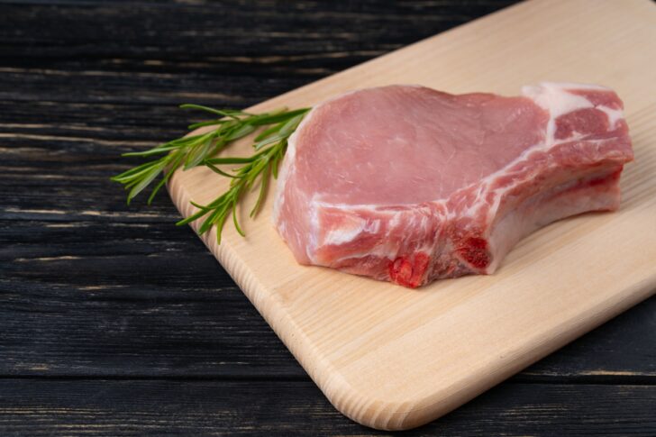 Top view of one pieces raw pork chop steaks with rosemary on a cutting board.