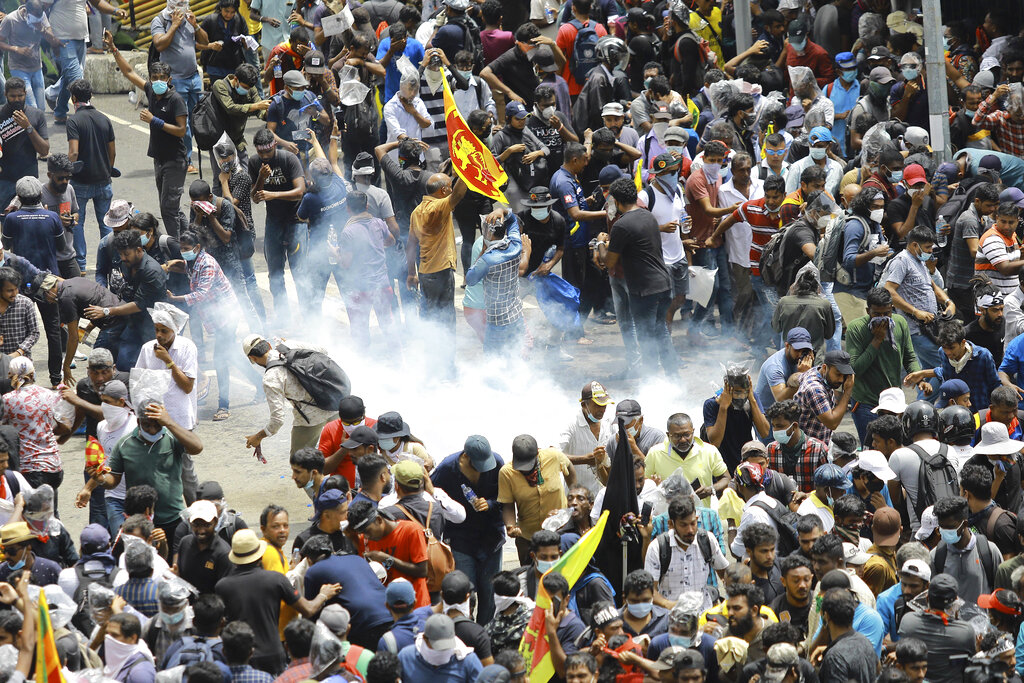 Protesters react as a tear gas shell fired by police lands next to them in Colombo, Sri Lanka, Saturday, July 9, 2022. Sri Lankan protesters demanding that President Gotabaya Rajapaksa resign forced their way into his official residence on Saturday, a local television report said, as thousands of people took to the streets in the capital decrying the island nation's worst economic crisis in recent memory.