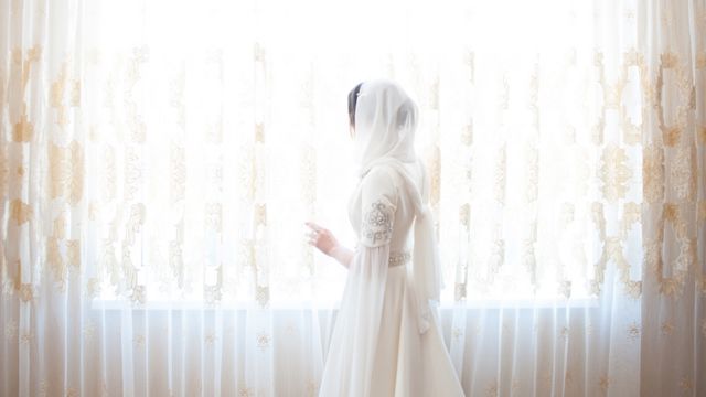Woman in wedding dress looks out of window