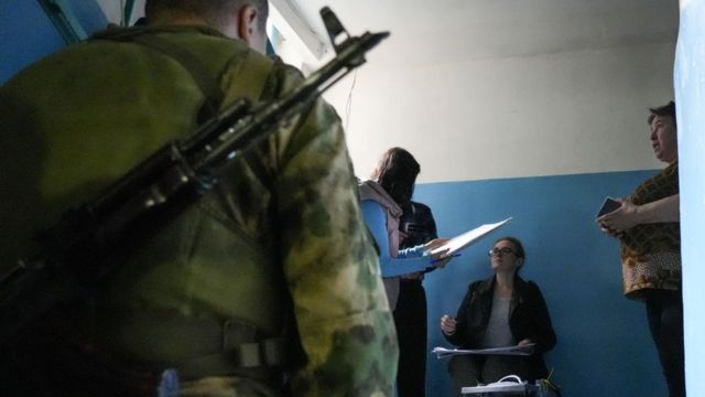 A soldier with a gun strapped across his back oversees 'referendum' officials in Donetsk on 23 September