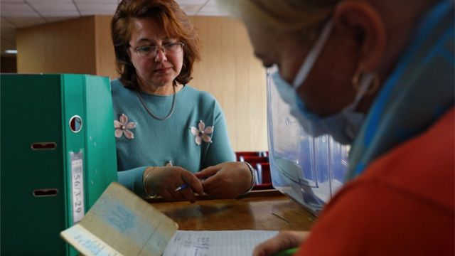 A woman wearing a mask checks another woman's passport to verify her identity for the so-called referendum in Mariupol