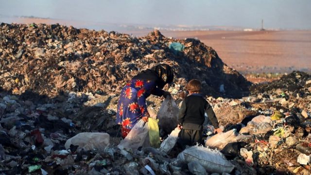 a woman and a child pick rubbish on a dump