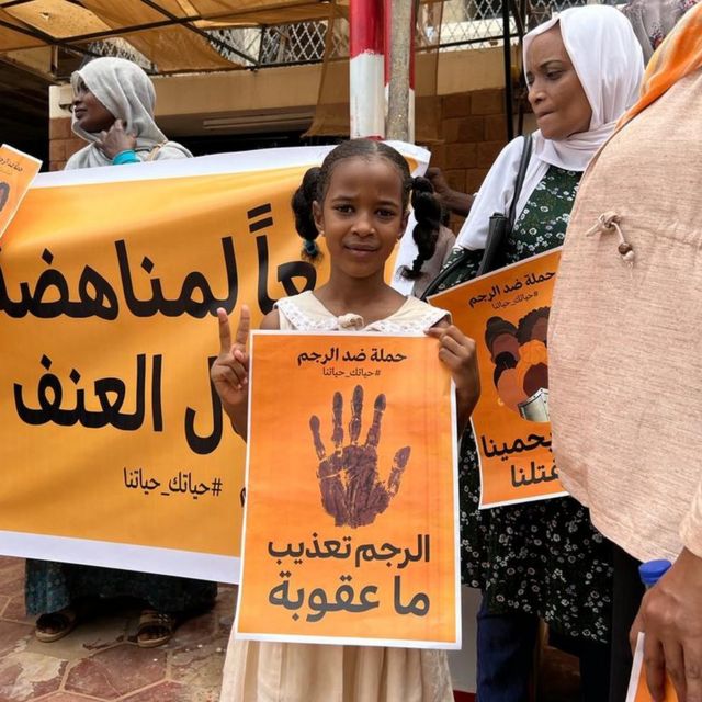 Protesters in Khartoum with posters saying "Stoning is torture, but where is the punishment?"
