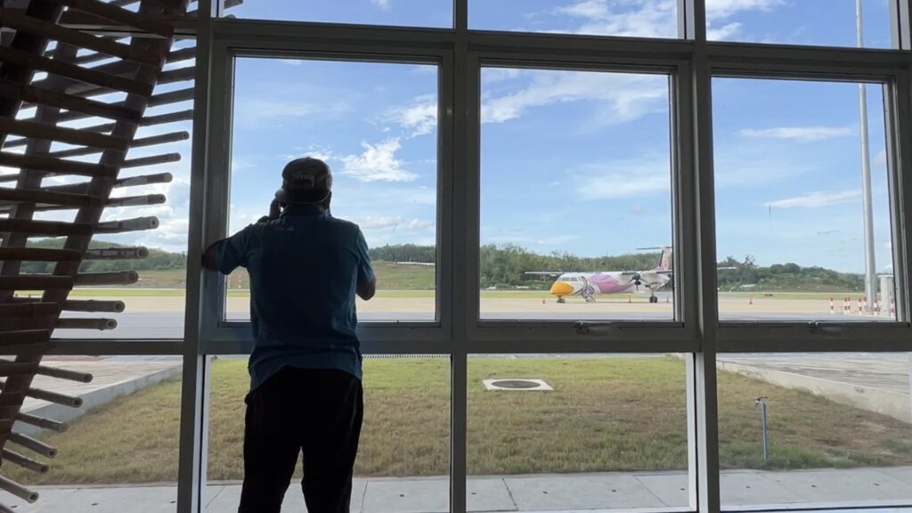 ชายกำลังยืนมองเครื่องบิน Q400 สายการบินนกแอร์ จากด้านในอาคารผู้โดยสารสนามบินเบตง