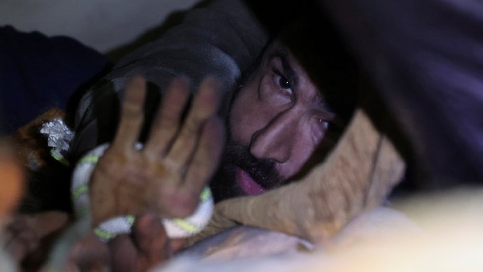 Abdulalim Muaini holds onto a rope as rescuers try to pull him out from under the rubble, in the aftermath of a deadly earthquake in Hatay, Turkey, February 8, 2023.