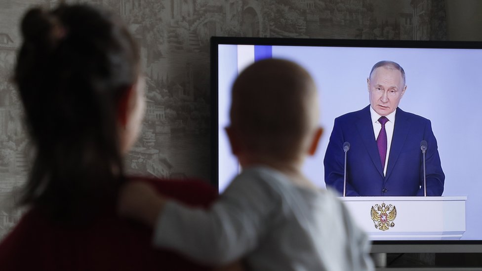 A woman holds her child as she watches the televised address by Russian President Vladimir Putin before the Federal Assembly, in Moscow, Russia, 21 February 2023. '