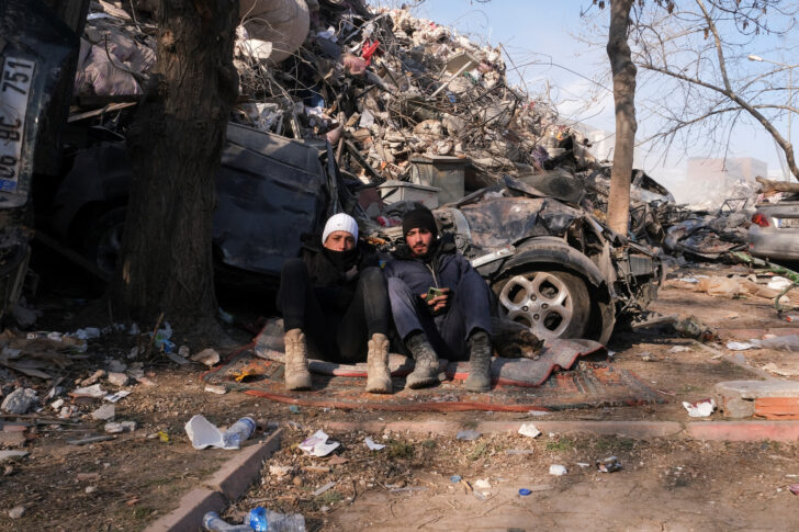 Two boys sit on the ground surrounded by debris in Maras