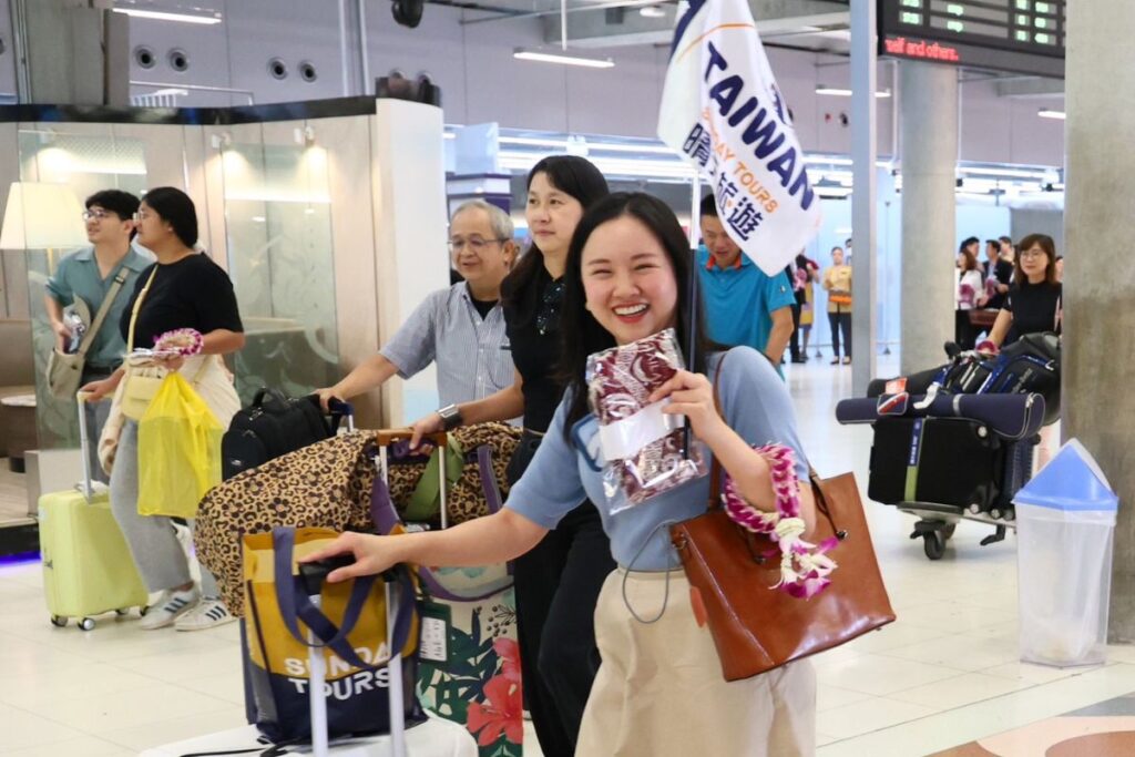 ผู้โดยสารเที่ยวบิน CI 835 สายการบิน China Airlines ในมือถือธงบริษัททัวร์ ปรากฏคำว่าไต้หวัน ยิ้มให้กับกล้อง