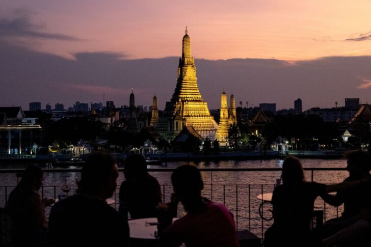 TOURISM-WAT ARUN 5 ผู้คนนั่งอยู่บนบาร์ และมองไปยังพระปรางค์วัดอรุณราชวรารามราชวรมหาวิหาร ซึ่งอยู่ฝั่งตรงข้าม ในบรรยากาศยามเย็น มีแม่น้ำเจ้าพระยาคั่นกลาง
