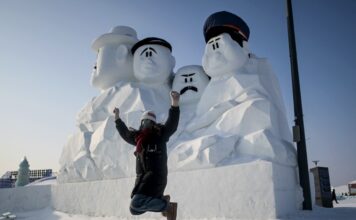 นักท่องเที่ยวกระโดดเพือ่ถ่ายภาพกับหิมะแกะสลักเป็นหน้าคนขนาดใหญ่