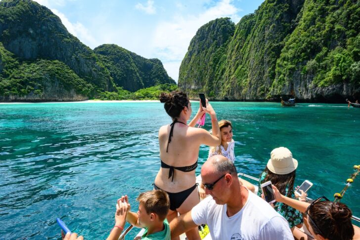 นักท่องเที่ยวหลายคนถ่ายภาพอ่าวมาหยา เกาะพีพี บนเรือ ก่อนถึงแนวกั้นกำหนดโดยกรมอุทยานแห่งชาติ สัตว์ป่า และพันธุ์พืช