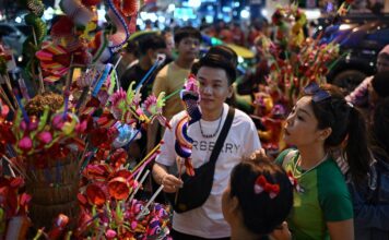 นักท่องเที่ยวกำลังเลือกชมหุ่นมังกรกระดาษบนถนนเยาวราช ท่ามกลางผู้คนที่เดินไปมามากมาย ก่อนวันตรุษจีน 2024