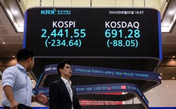 ผู้คนเดินผ่านหน้าจอมอนิเตอร์ที่แสดง KOSPI ดัชนีราคาหุ้นแบบผสมของเกาหลี และ KOSDAQ ดัชนีที่สะท้อนการเคลื่อนไหวของหุ้นขนาดกลาง-ขนาดเล็กในเกาหลีใต้ ณ วันปิดตลาดที่ 5 สิงหาคม (ภาพโดย ANTHONY WALLACE / AFP)