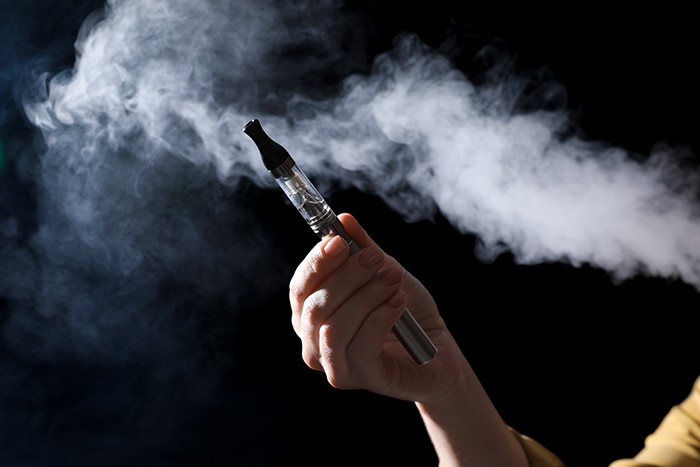 Woman holding electronic cigarette on black background, closeup